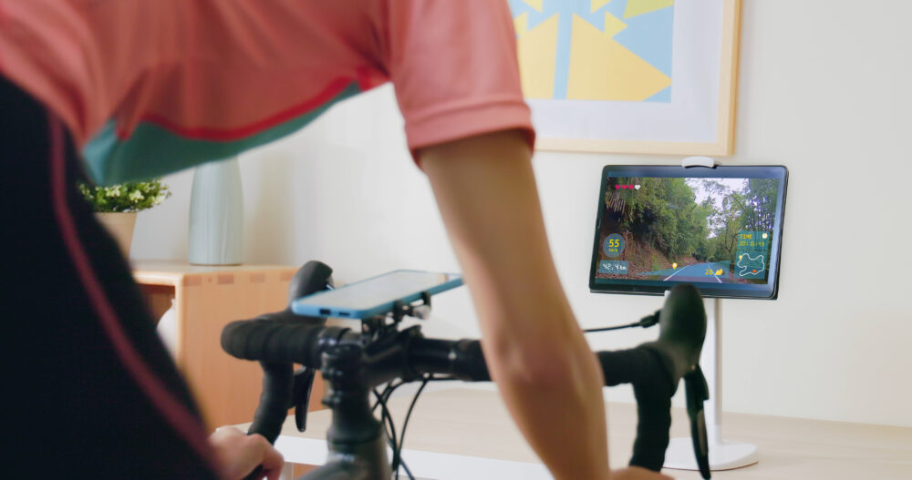 Photo of woman on an indoor bike doing virtual cycling on a computer screen.  Virtual cycling can be a quick and easy way to get back into cycling when you've had a baby