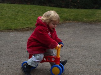 Review to find out how fast can a kid go on a toddler bike - the image shows the Lena My First Scooter being ridden by a two year old with blond hair. They are picking up speed and have both their feet off the ground