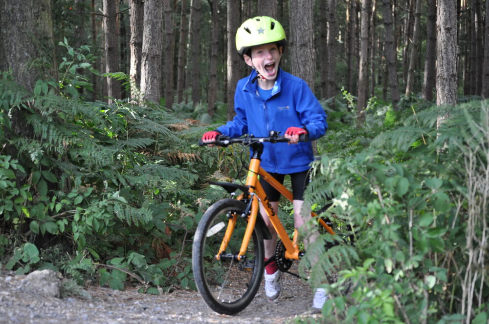 Best kids' bikes: A child standing over a Frog bike looking very excited, surrounded by ferns