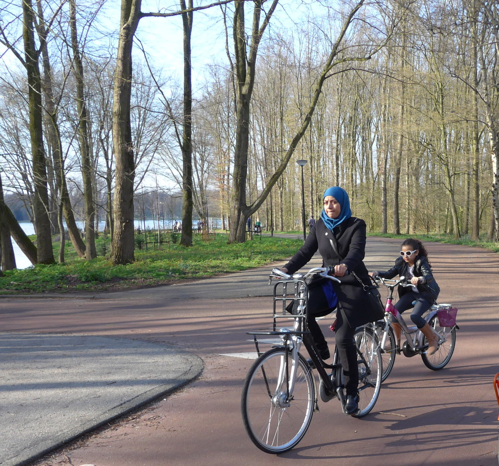 Photo of woman in headscarf and child cycling bikes