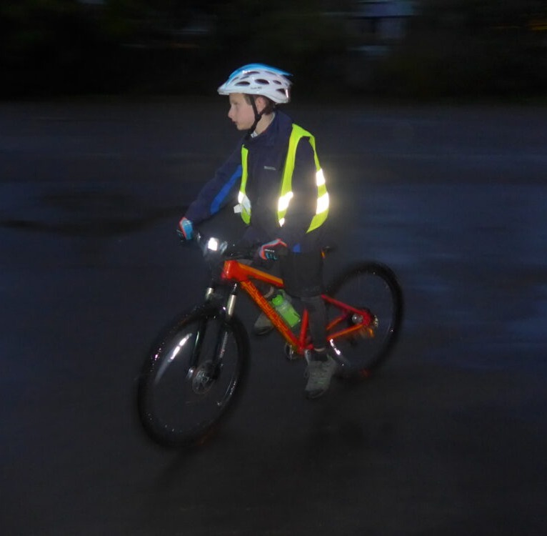 Winter cycling with kids: A boy on his bike in the dark, with a front light and a reflective jacket