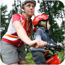 A parent cycling with a toddler in a front-mounted bike seat, seen from the side and up close