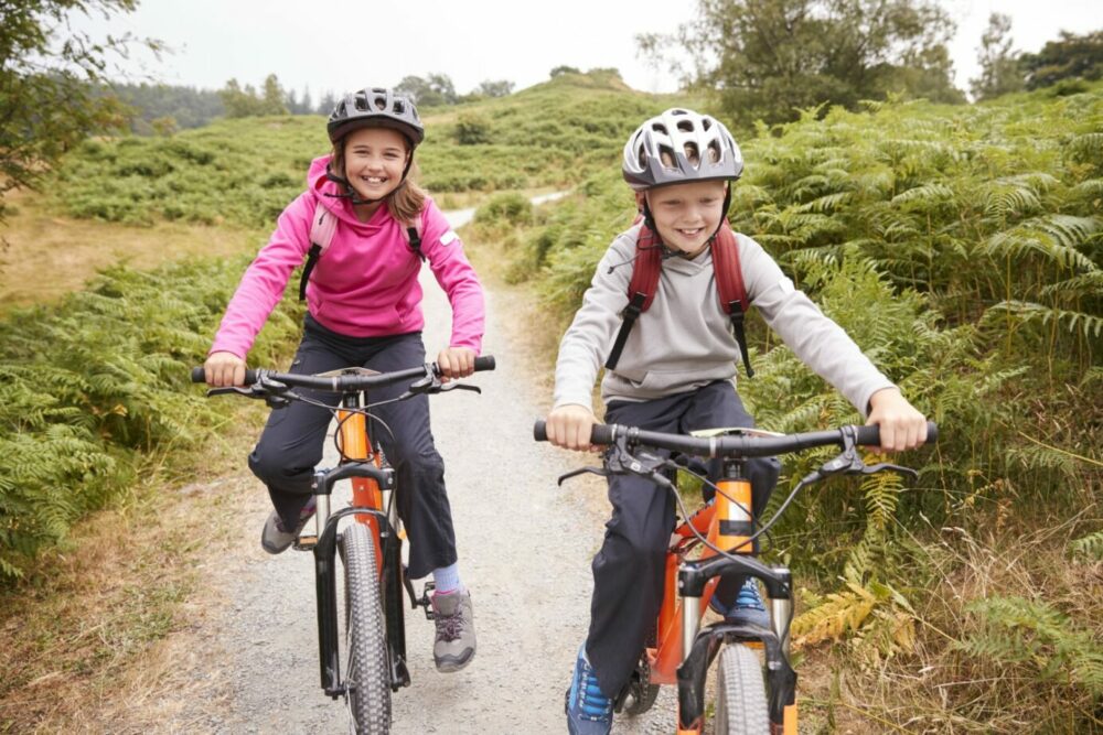 How to choose the right size kids' bike: Two children cycling side by side towards the camera, smiling