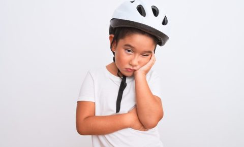 Boy wearing white cycling helmet not wanting to ride his bike