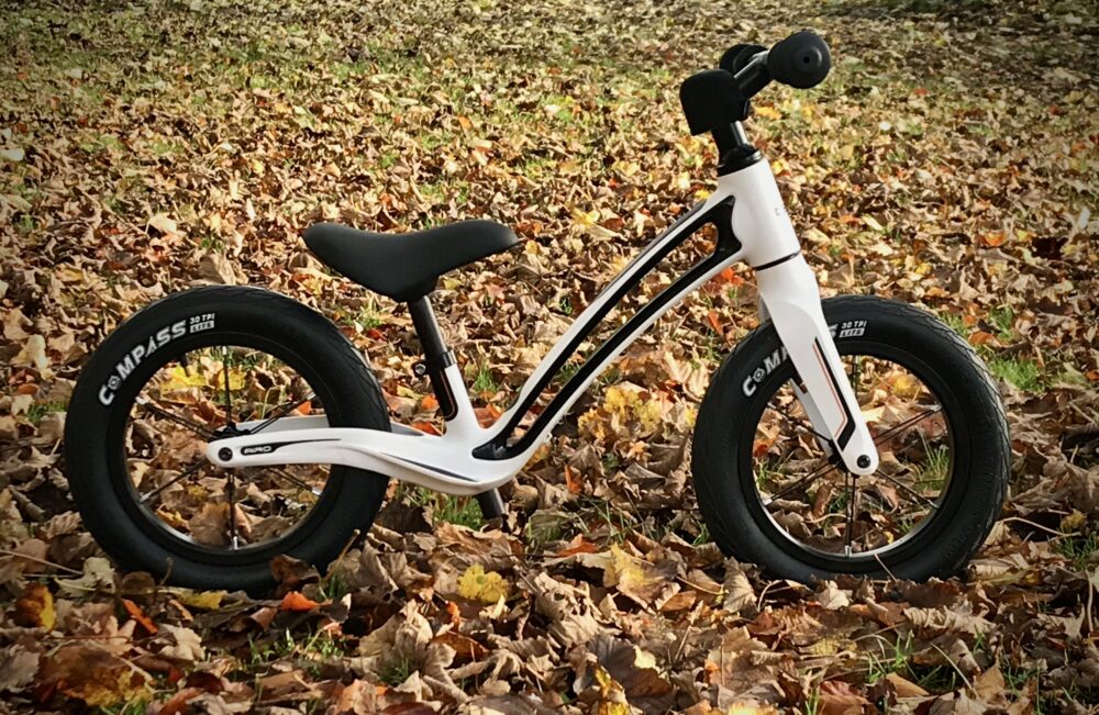 The Hornit Airo balance bike photographed in the autumn with lots of leaves around it.  It's a great balance bike for riding all year round