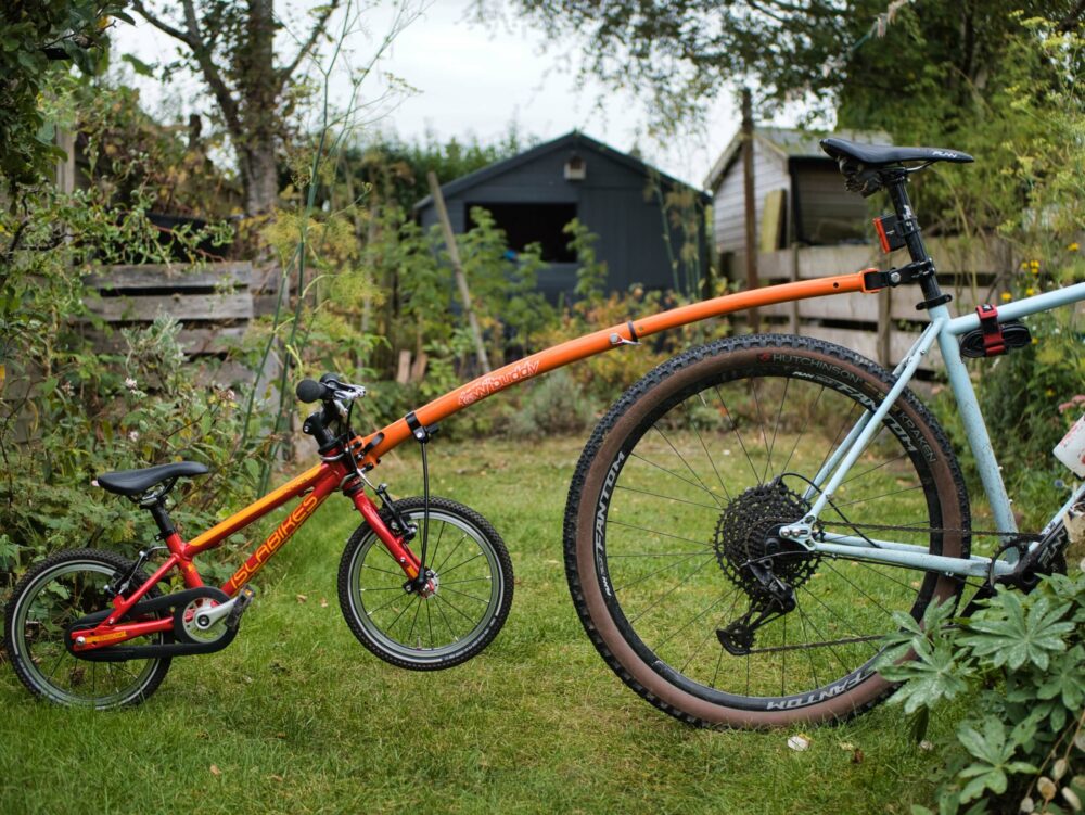 An adult's bike with a child's bike hitched to the back via a towbar