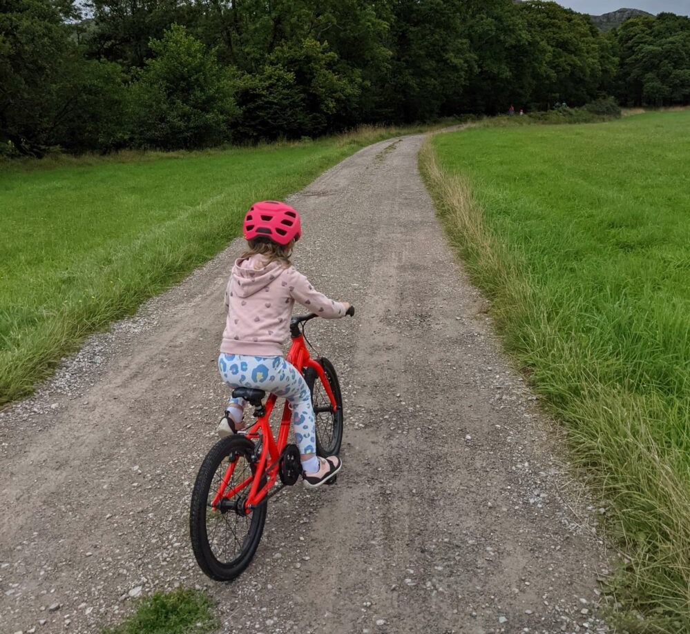 How to choose the right size kids' bike: A girl seen from behind riding a bike on a gravel path