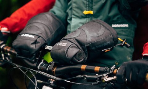 Photo of Kids Ride Shotgun Pogies for keeping little hands warm during winter on a front bike seat - photo of a close up of child's hands inside the black pogies with green jacket tucked inside