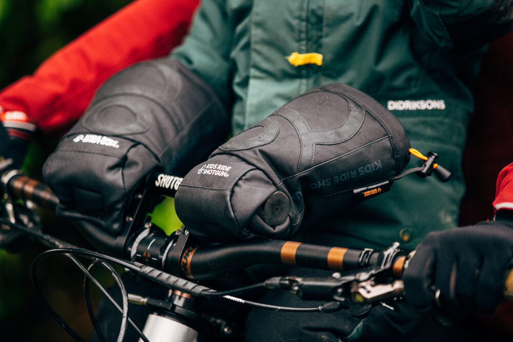 Photo of Kids Ride Shotgun Pogies for keeping little hands warm during winter on a front bike seat - photo of a close up of child's hands inside the black pogies with green jacket tucked inside