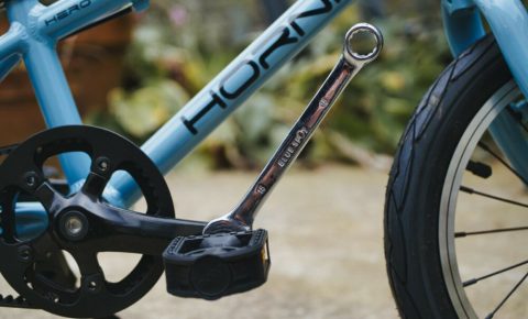 Photo of a blue Hornit Hero 14 kids bike with a spanner on the drive side pedal about to be taken off to turn it into a balance bike