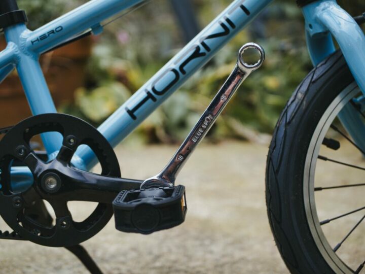 Photo of a blue Hornit Hero 14 kids bike with a spanner on the drive side pedal about to be taken off to turn it into a balance bike