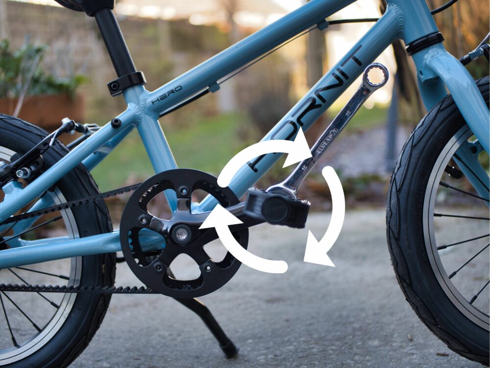 Photo showing the right hand pedal being put back onto a kids bike and arrow showing which is the correct way to tighten the pedal