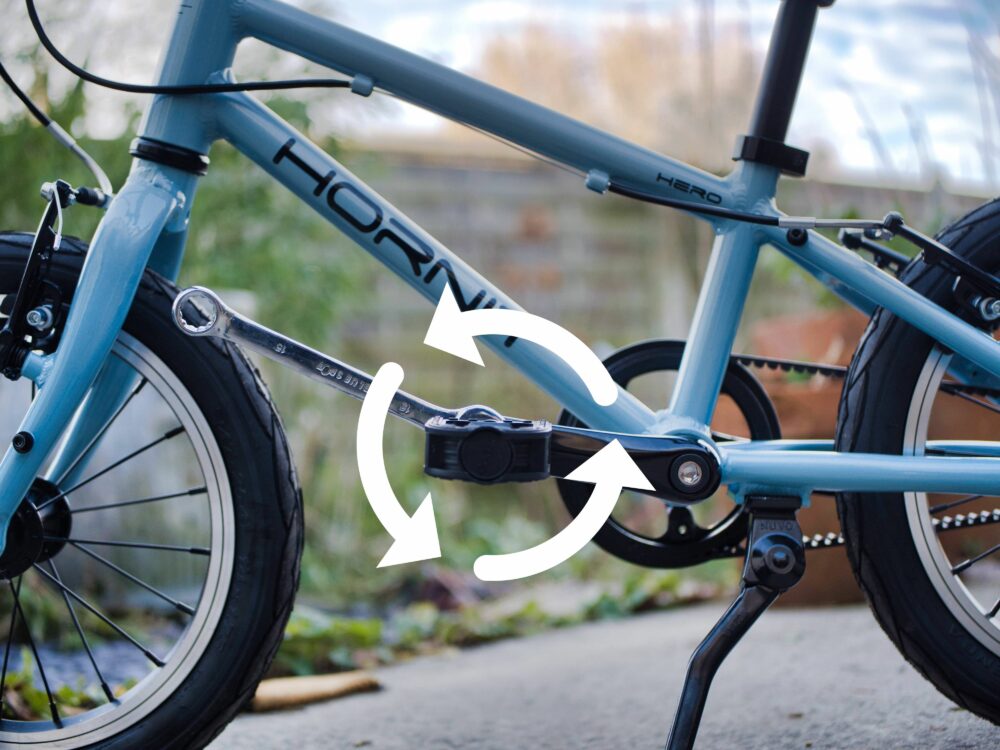 Photo of bike having pedal being put back on the non drive side showing which way to turn them with arrow showing direction of travel of spanner