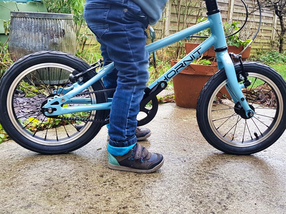 Photo of 3 year old child sitting on a pedal bike with the pedals removed, demonstrating the saddle position needed for balance biking