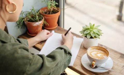 Woman sit at office surround with green plants, coffee and write at her note book