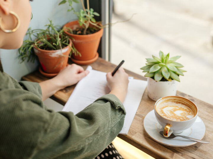 Woman sit at office surround with green plants, coffee and write at her note book