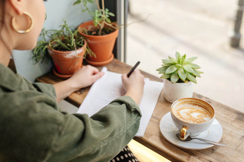 Woman sit at office surround with green plants, coffee and write at her note book