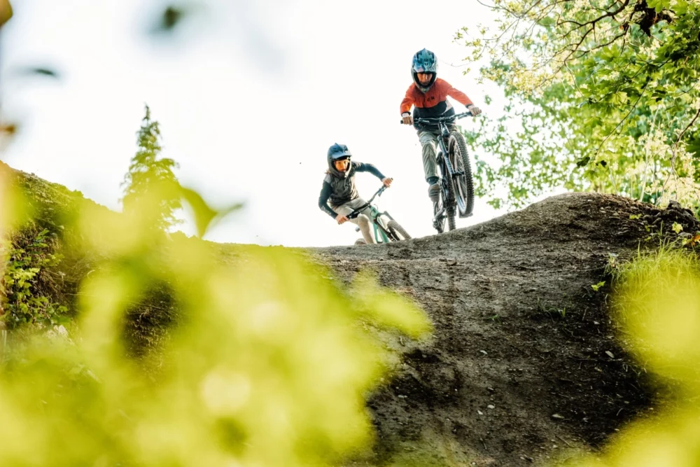 Best kids' full-suspension mountain bikes: Two kids riding full suspension mountain bikes in full face helmets.