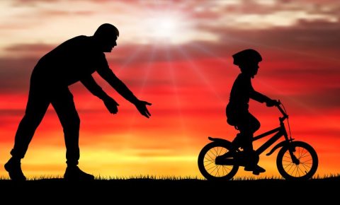 Silhouette of parent teaching child to ride a bike