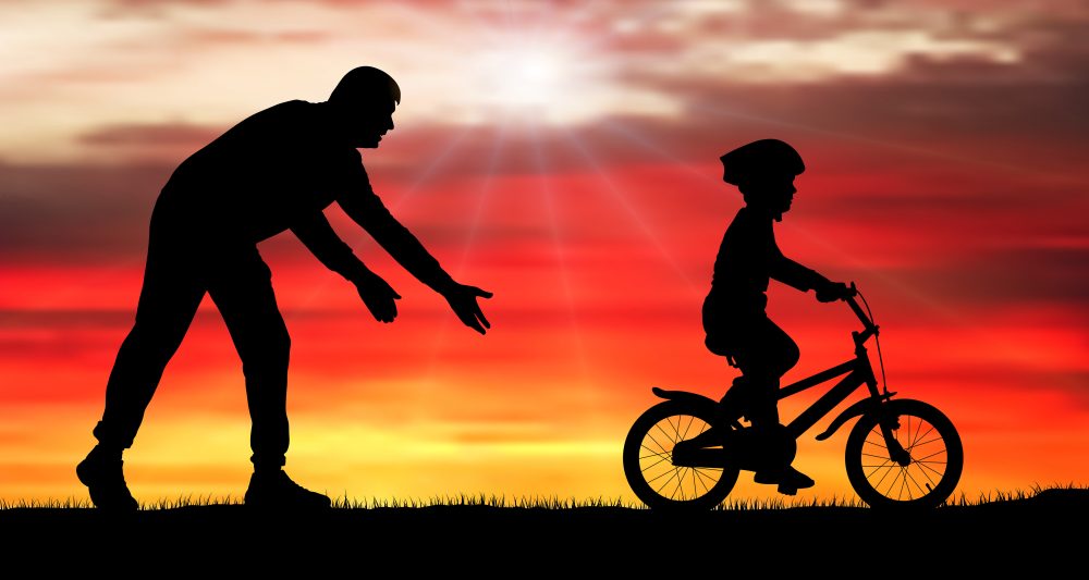 Silhouette of parent teaching child to ride a bike