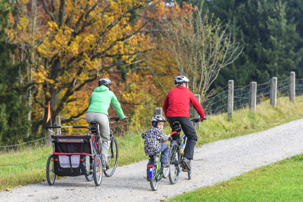 Tagalong kids bike Two parents cycling side by side, one with a trailer and one with a child on a tagalong