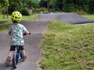 A toddler seen from behind riding a balance bike on a pump track