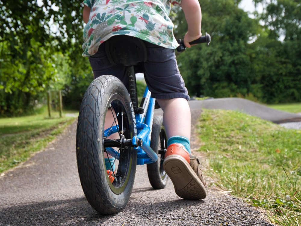 How to choose the right size kids' bike: Close up of a toddler's leg while riding a balance bike on a pump track