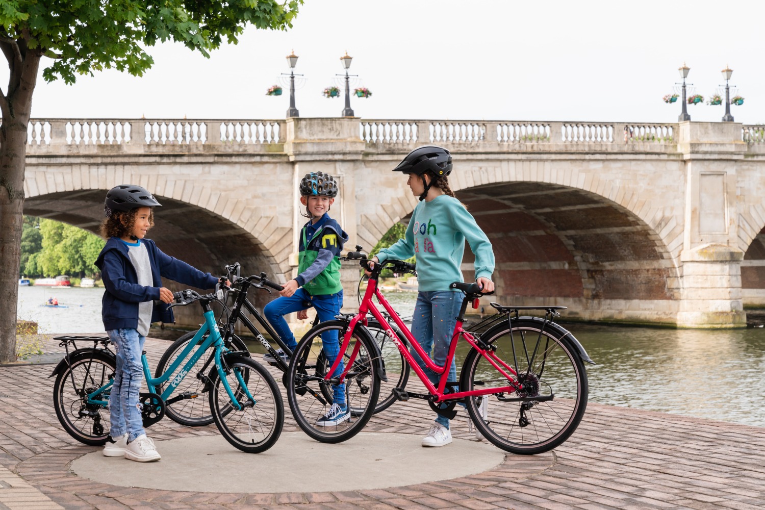 Best 26" kids' bikes: Three children with step-through city bikes chatting in front of a bridge