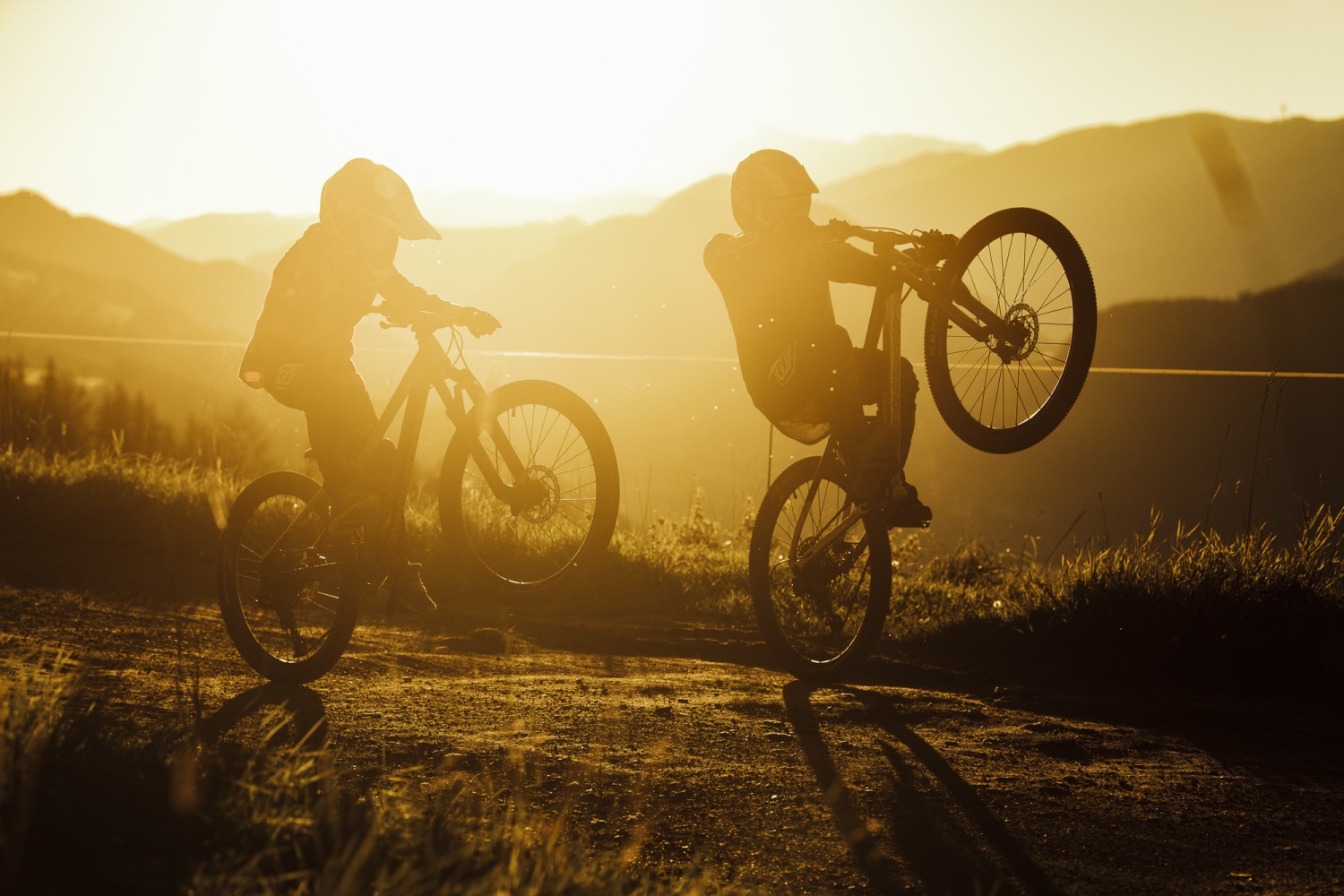 Best kids' full-suspension mountain bikes: Two children wheelie-ing their mountain bikes in front of a golden hour landscape