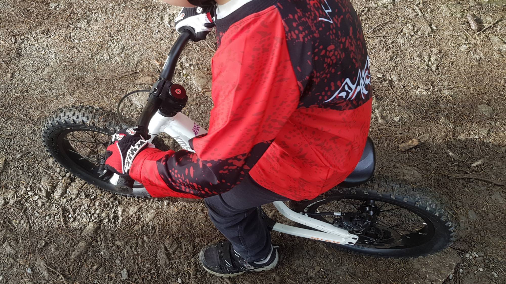 Little boy in a red top riding the dirt hero balance bike