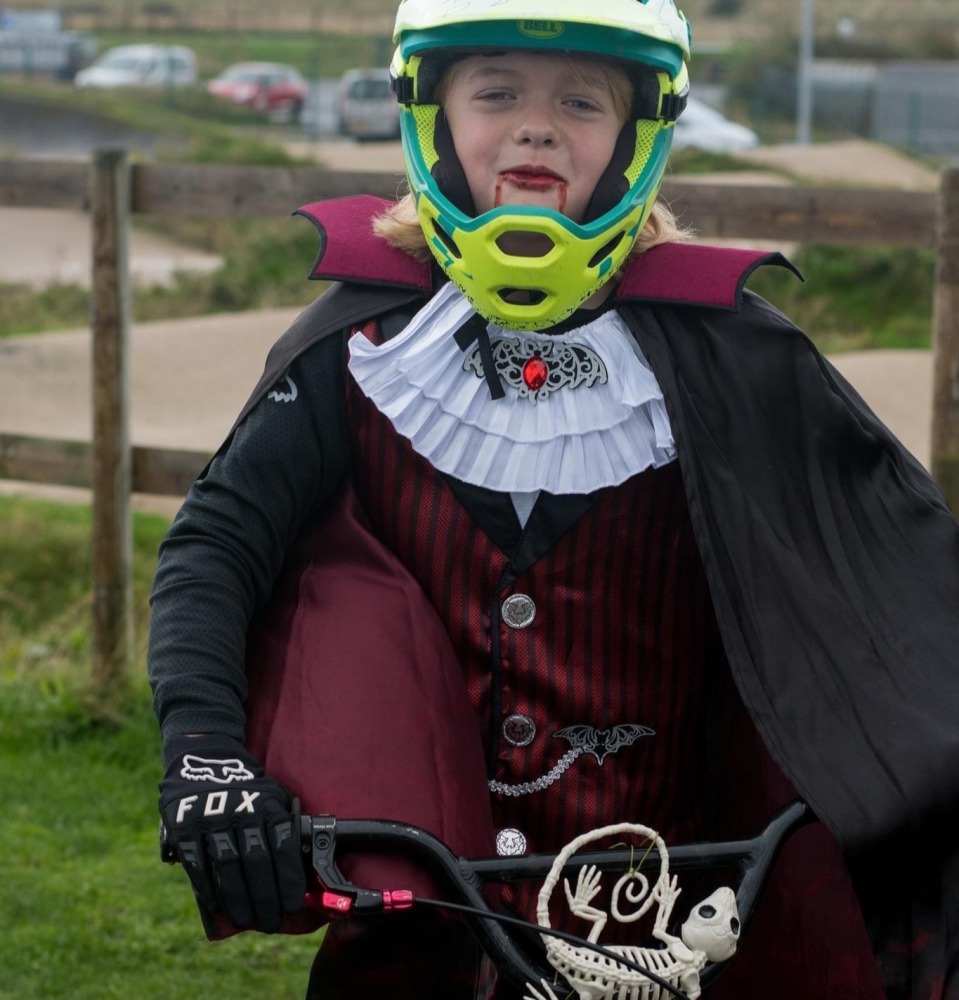 Halloween Costumes for Cycling Kids: A young child in a Vampire costume and full face mountain biking helmet, riding a bike