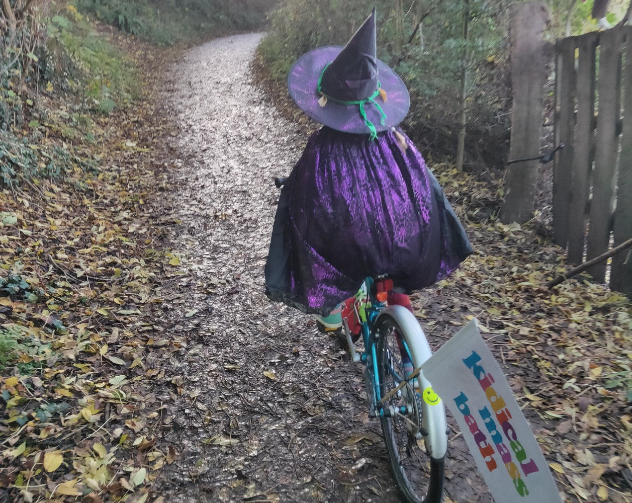 Halloween Costumes for Cycling Kids: A young girl pictured from behind riding a bike in a witch costume.