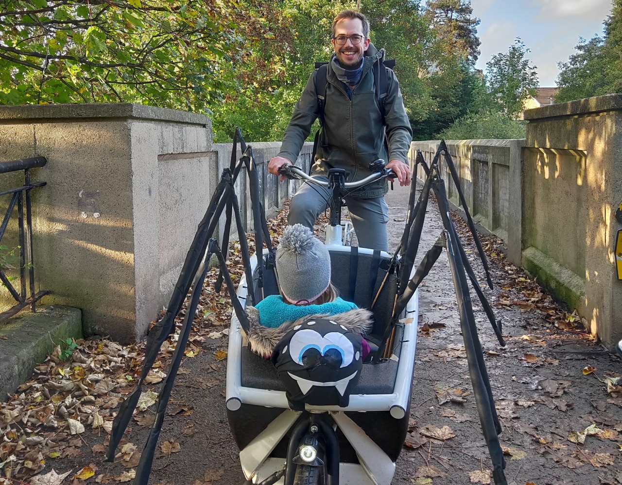 Halloween Costumes for Cycling Kids: A man carrying a child in a cargo bike that's been decorated to look like a giant spider.