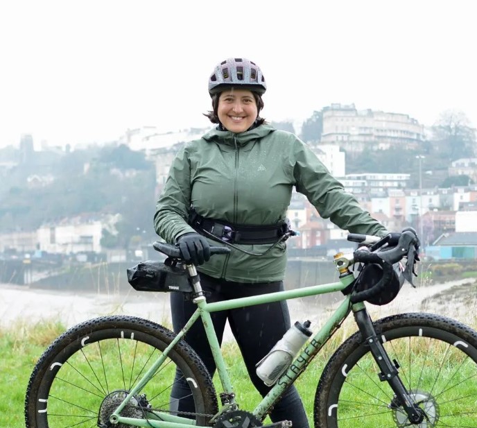 Mildred Locke, standing next to a green Stayer gravel bike in front of the river Avon in Bristol
