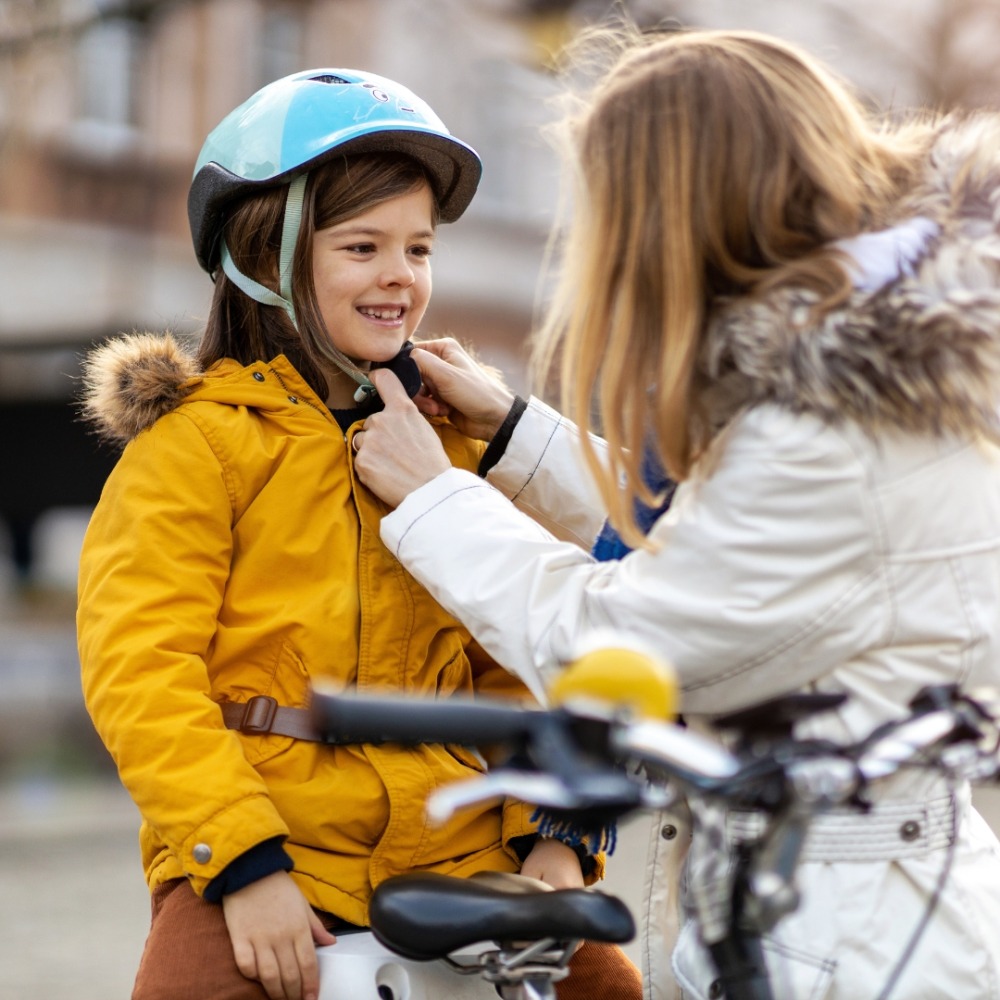 Winter cycling with kids: A woman buckling up her daughter's bike helmet