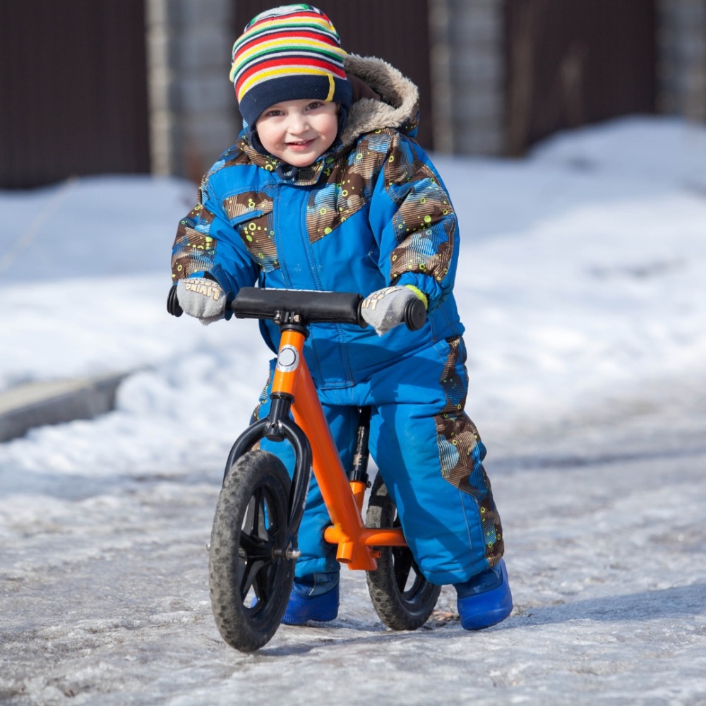 Winter cycling with kids: a toddler on a bike in a snowy street wearing a big puddle suit for warmth