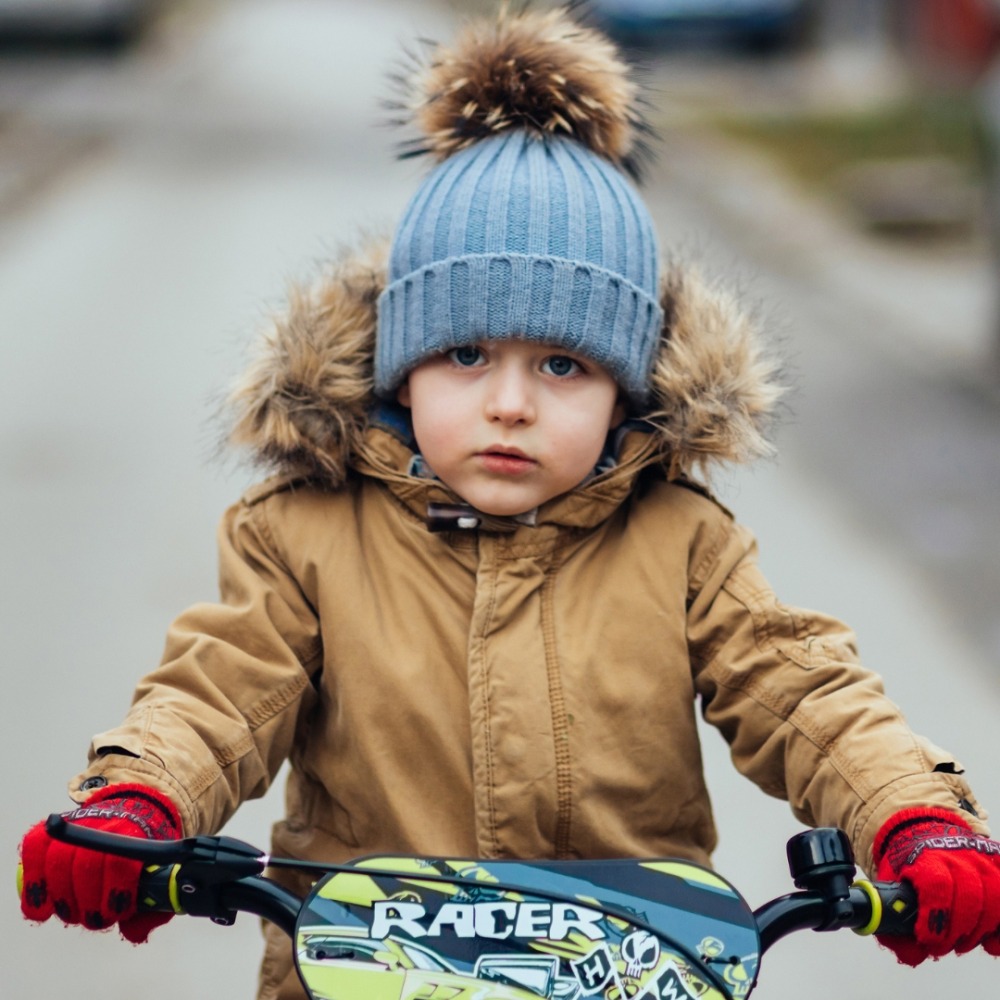 Winter cycling with kids: A little boy on his bike facing the camera wearing a Parker coat and a bobble hat