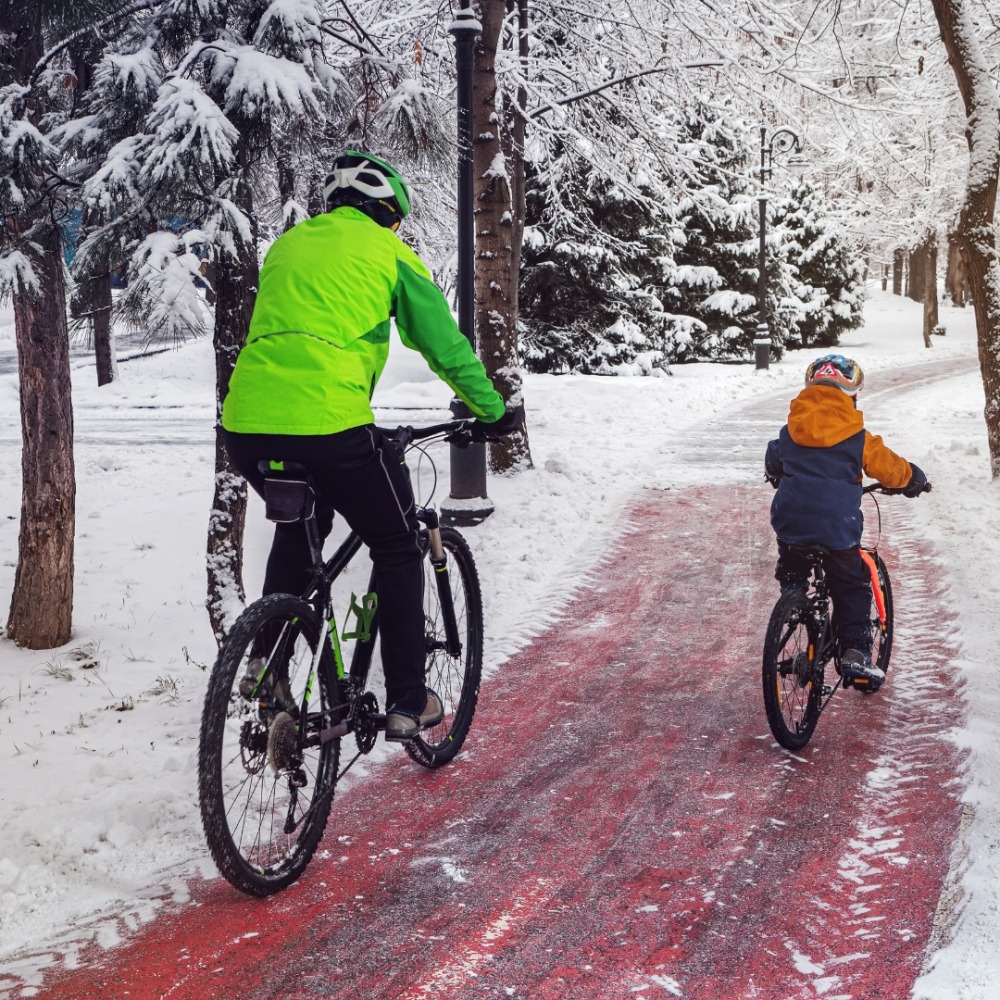 Winter cycling with kids: A father and child cycling in the snow, wearing hi-viz jackets