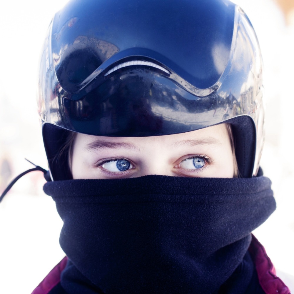 Winter cycling with kids: A close up of a girl wearing a bike helmet and a snood around her face so only her eyes are visible