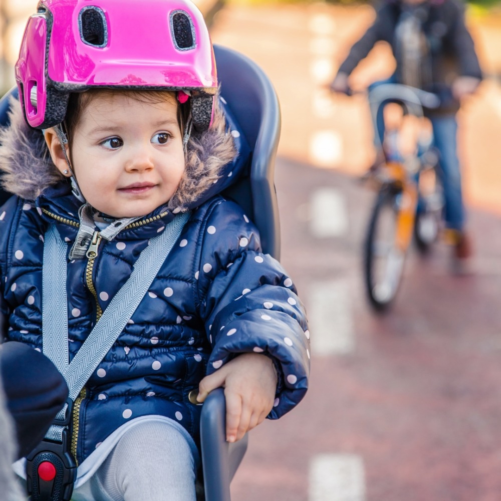 Winter cycling with kids: A toddler wearing a bike helmet and sitting in a child seat at the rear of a bike
