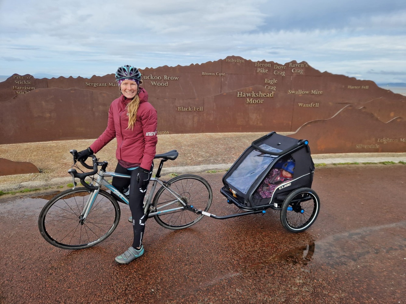 A woman riding a road bike with a trailer attached to the back