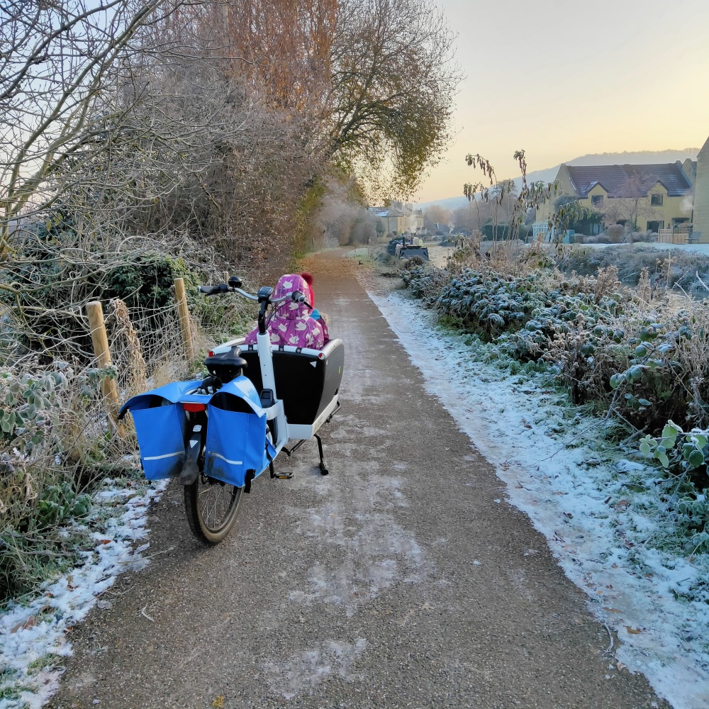 Winter cycling with kids: A cargo bike seen from behind, parked up on a wintry path with children sitting in the front