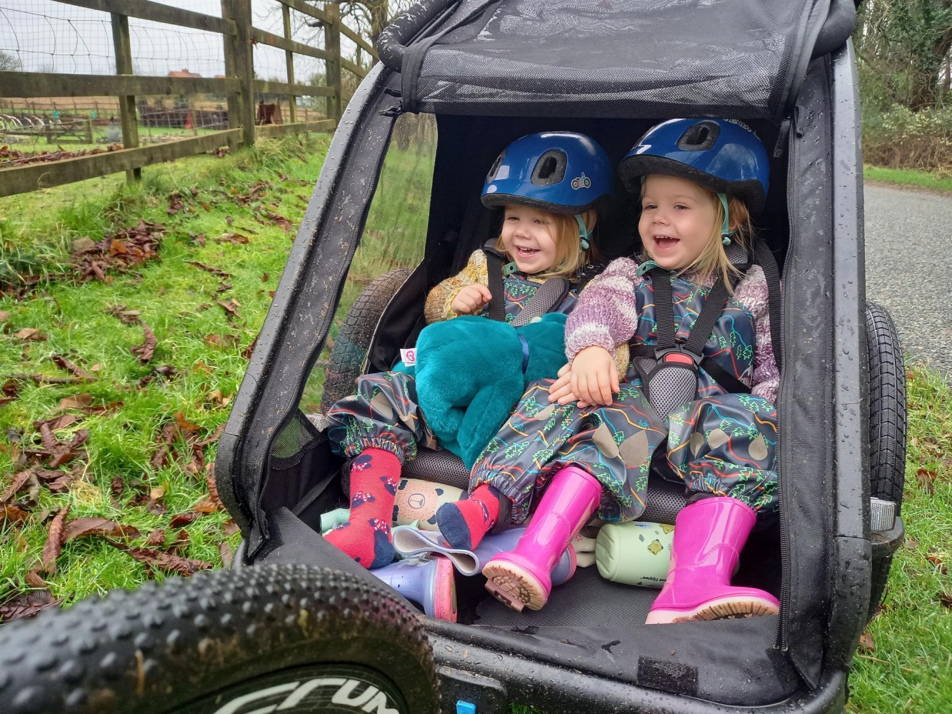 Two twin girls laughing and smiling in a bike trailer