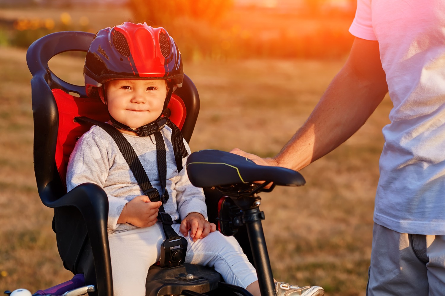 A toddler wearing a bike helmet, in a rear bike seat, smiling