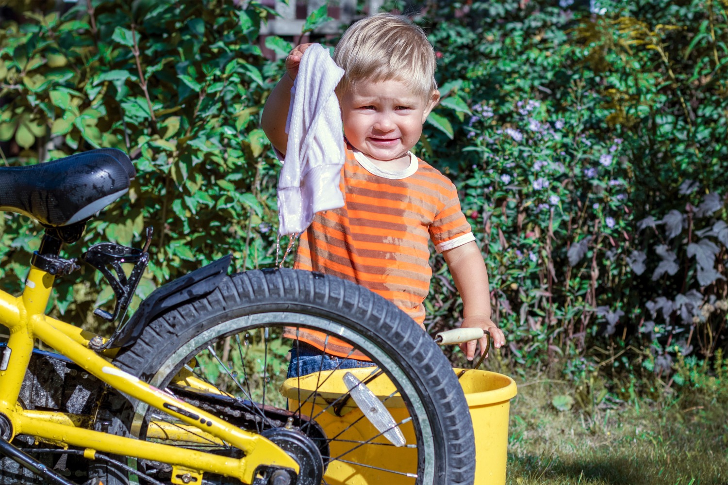 little boy in an orange top cleaning his yellow bike