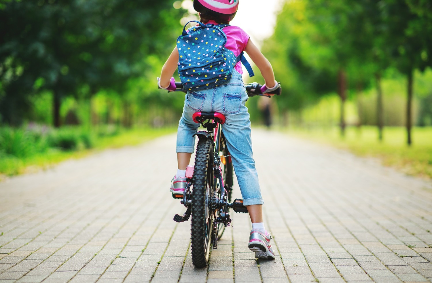 A young girl on her bike, with a backpack, seen from behind