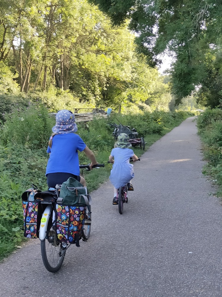 How to choose the right size kids' bike: Two children seen from behind, cycling their bikes along a traffic-free cycle path surrounded by trees
