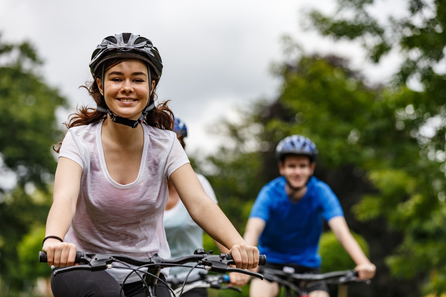 Best 26" hybrid bikes for kids - Two young teenagers cycling towards the camera, wearing helmets and smiling