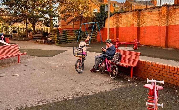 Cycling in Ramadan - A Muslim woman wearing a Hijab under her bike helmet, checking her phone on a park bench surrounded by her family's bikes