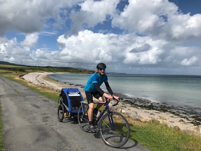 a man riding a road bike with panniers and a hired trailer at the seaside